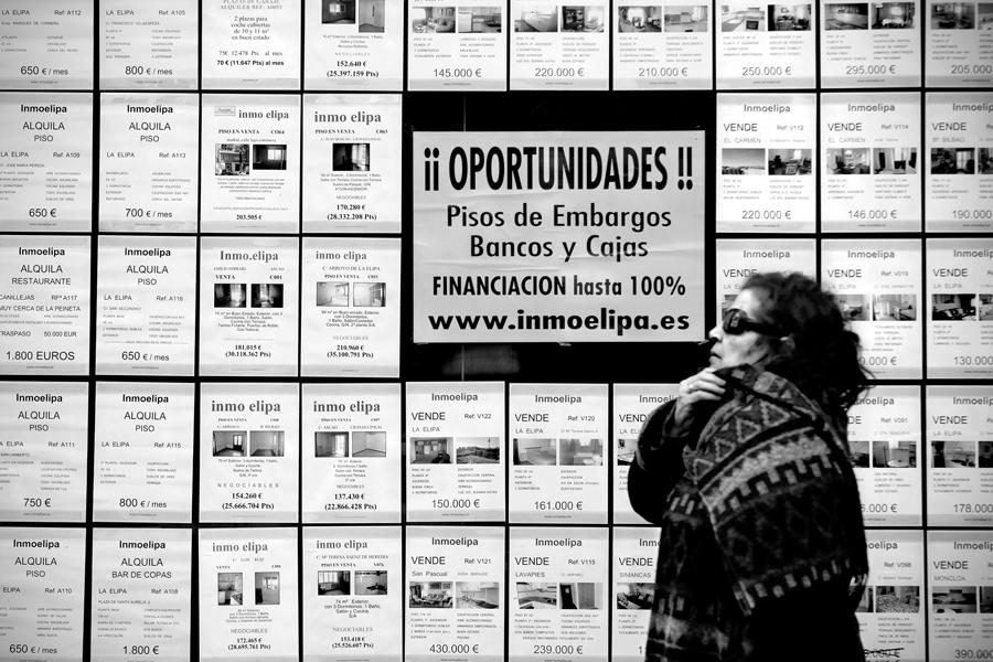 Una mujer pasa frente al escaparate de una inmobiliaria donde ofrecen pisos procedentes de desahucios. Barrio de la Elipa, Madrid, el 5 de marzo de 2011. Foto: Olmo Calvo